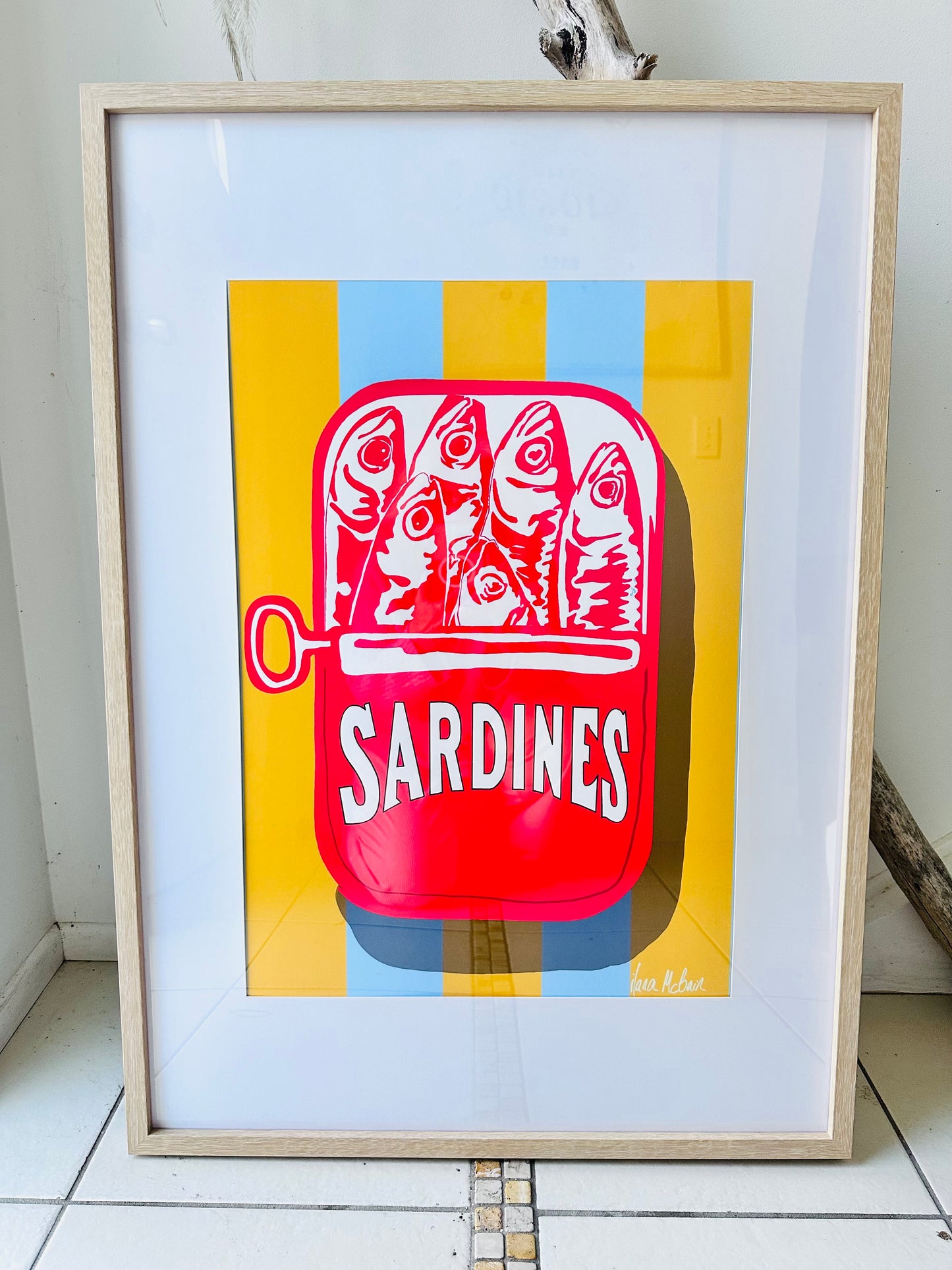 Framed artwork of a red sardine can with fish illustration on a yellow and blue striped background.