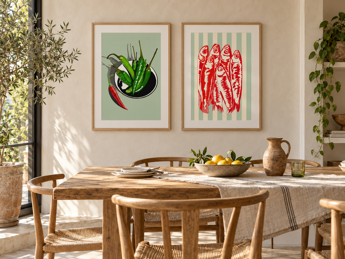 Mediterranean dining room with Riviera Sardines and Green Chillies art prints by Ilana McBain in natural birch frames above a rustic timber dining table.