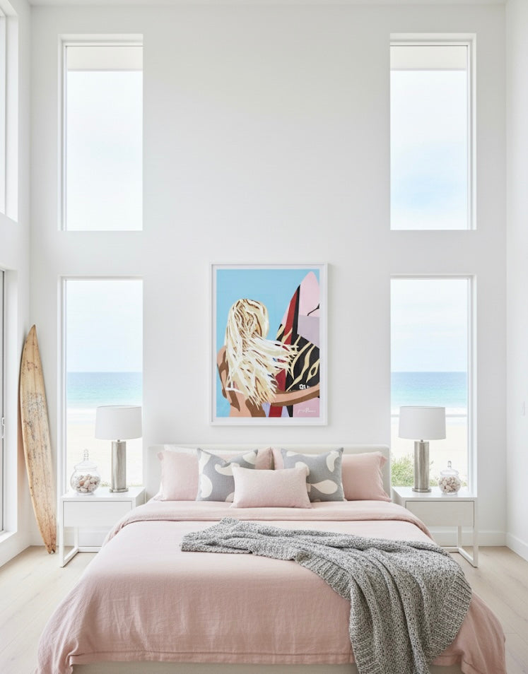 Framed art print of a woman with long blonde hair holding a colourful surfboard against a blue background a gallery on a white wall in a coastal bed room.