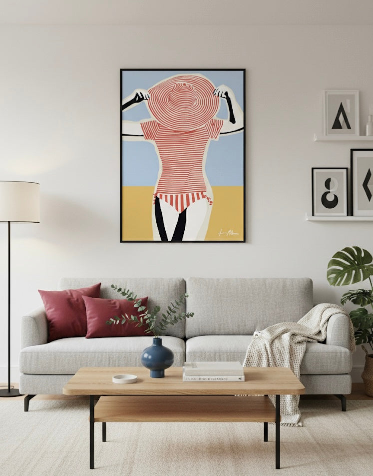 A gallery including an art print Illustration of a woman wearing a red and white striped swimsuit with a matching large hat against a blue sky and sand background on a living room wall.