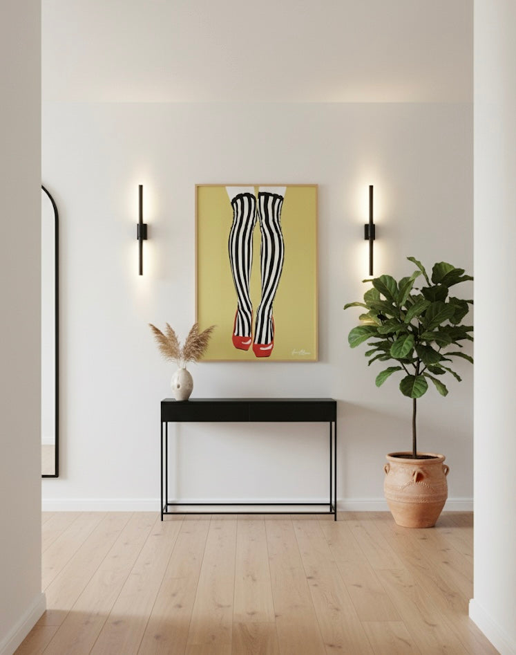 Modern interior with a console table, plant, and wall art of black and white striped tights with red shoes on a golden yellow background in a minimalistic setting.