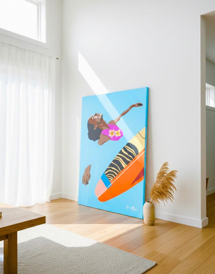 A vertical canvas painting depicting a bird's-eye view of a woman swimming in bright blue water. She has dark hair and wears a pink swimsuit with yellow flowers. An orange and yellow surfboard with a black zebra-stripe pattern floats diagonally beside her. Large stretched canvas print leaning on a modern room wall.