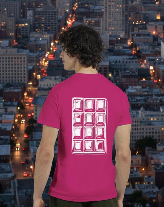 A model wearing a pink t-shirt with a chocolate bar white pop art, standing in front of a cityscape at night.