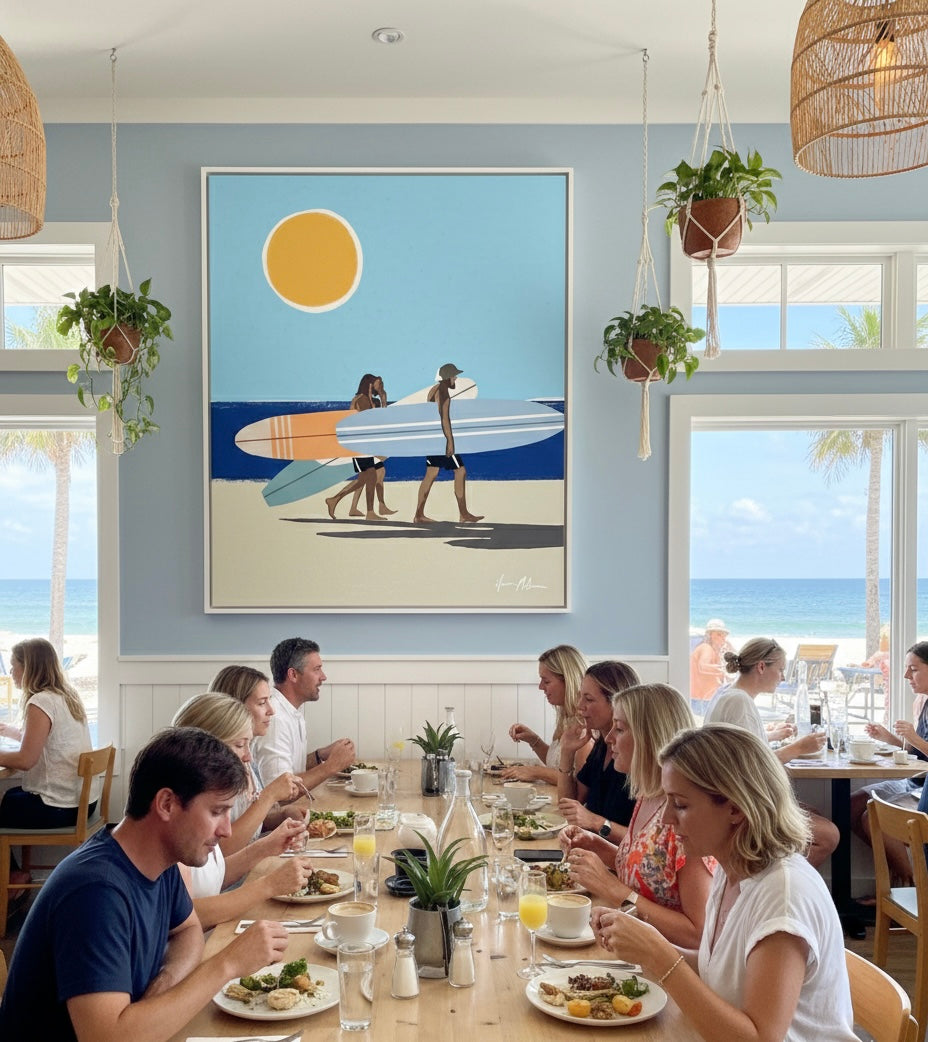 People dining at a restaurant with a large wall art of surfers with a surfboard. Wave Chasers limited edition canvas artwork by Ilana McBain inspired by ocean movement and adventurous coastal energy