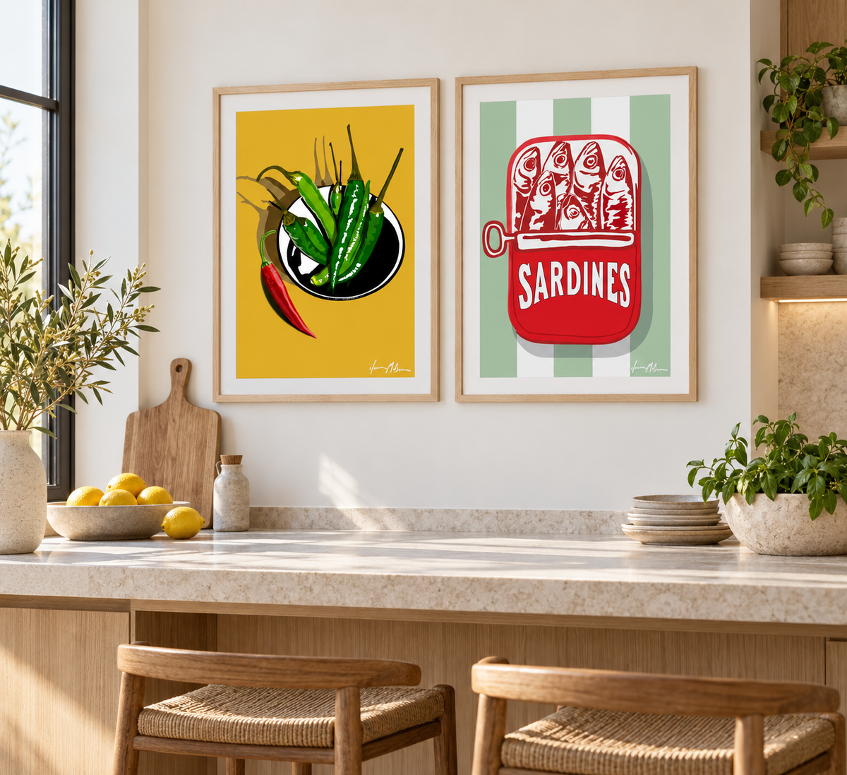 A Little Heat chilli art print and Riviera Sardines art print displayed side by side in a bright modern kitchen with natural timber cabinetry, stone surfaces and birch frames.