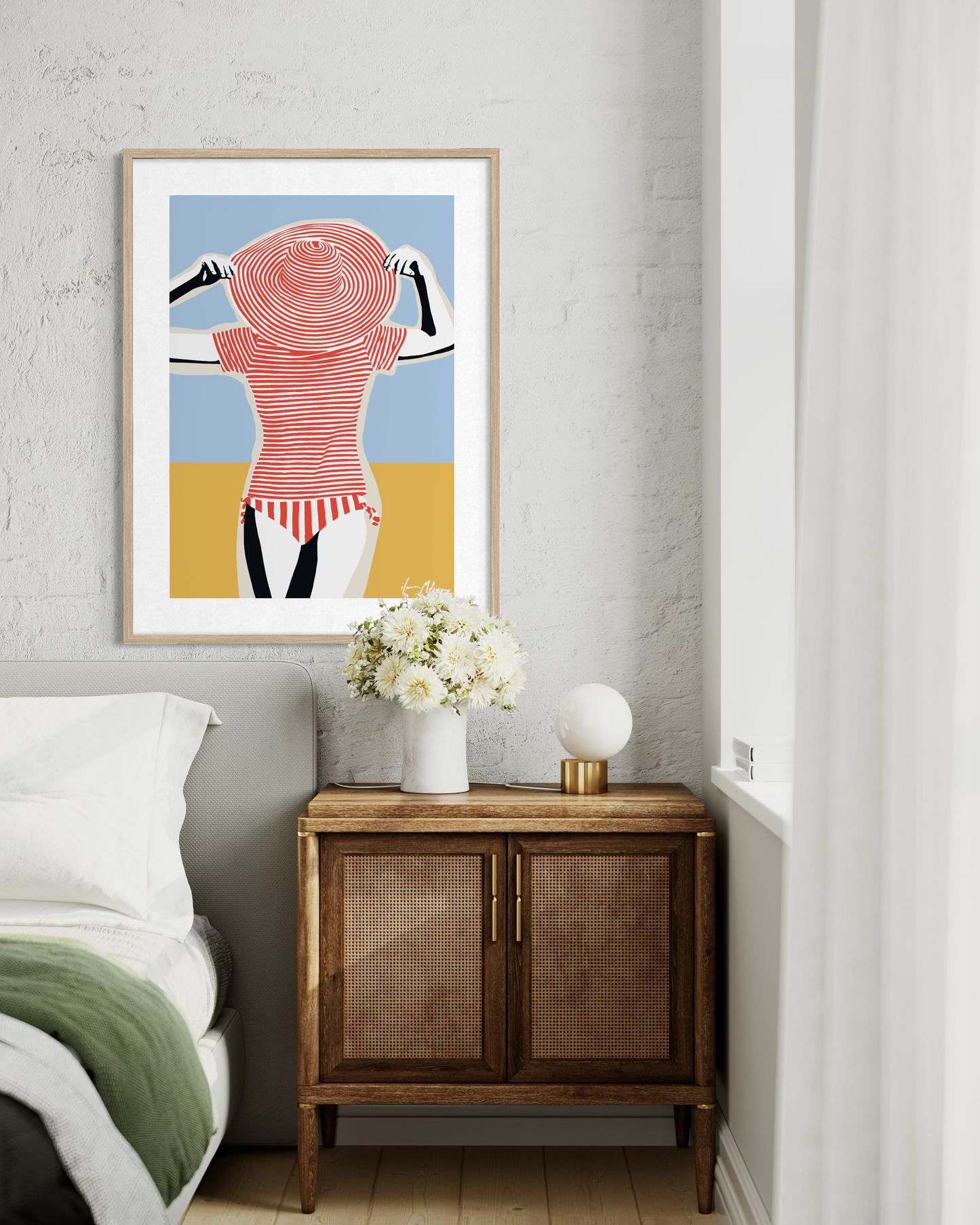 Contemporary retro beach artwork of a woman in striped swimsuit and sun hat by Australian artist Ilana McBain displayed as framed wall art in modern bedroom interior.